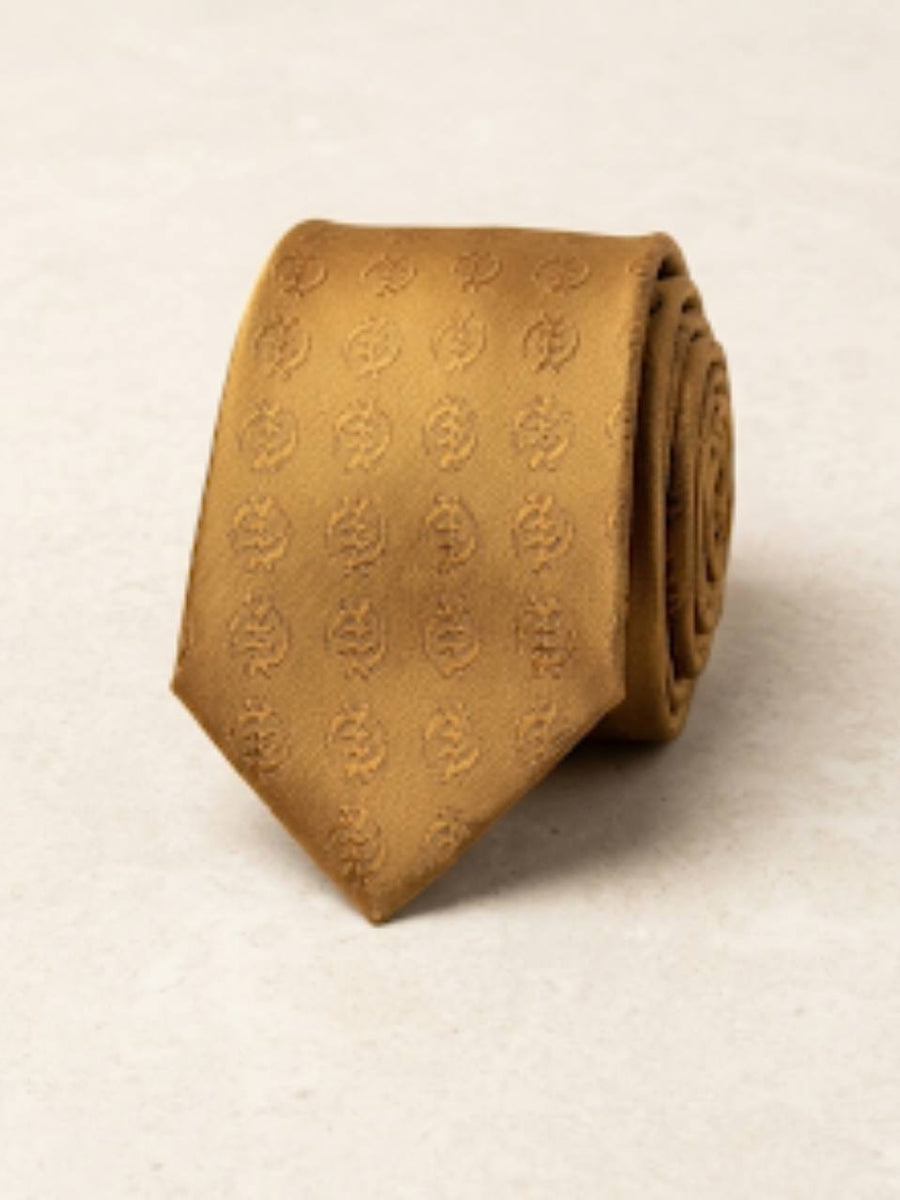 ODEHYE Golden Heritage Tie rolled on warm stone, showing repeated tonal Gye Nyame symbols